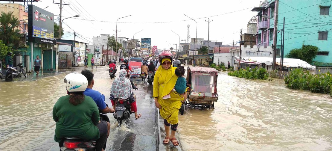 Ilustrasi seorang perempuan menggendong anaknya dan sejumlah pengendara melintas di lokasi banjir beberapa waktu lalu di Medan. Pengendara melintas di tengah cuaca mendung di Medan. BMKG mengimbau warga mewaspadai perubahan cuaca yang dipicu bibit siklon tropis.